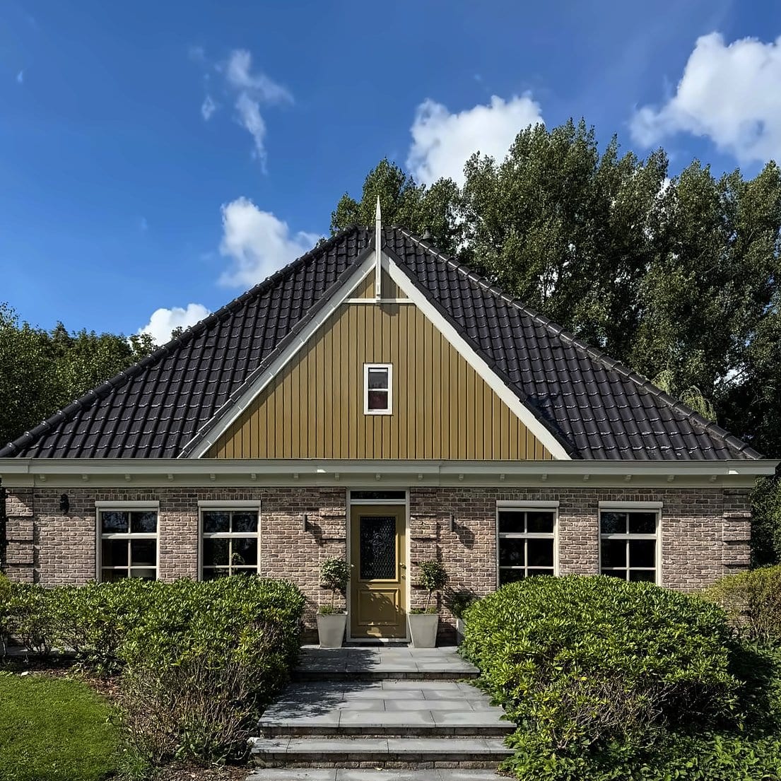Vrijstaande woning met okerkleurige houten topgevel, witte windveren en kozijnen